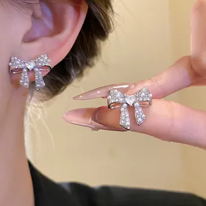 Elegant silver bow stud earrings with pearls and heart-shaped zircons shown on ear