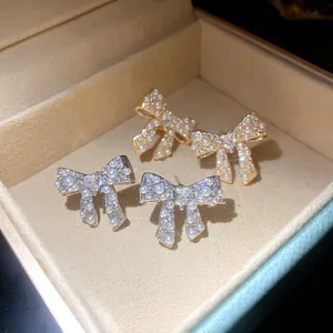 Close-up of elegant gold and silver bow stud earrings with pearls and zirconia
