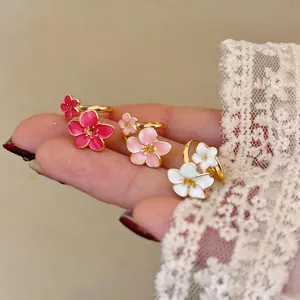 Vista dettagliata di tre eleganti anelli a fiore in smalto rosa, bianco e oro.