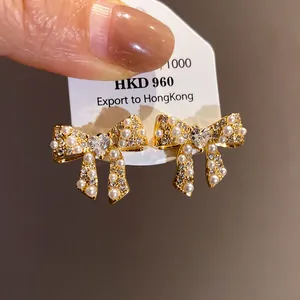 Macro detail showing 18k gold-plated bow earrings with pearls and a heart-shaped zircon.