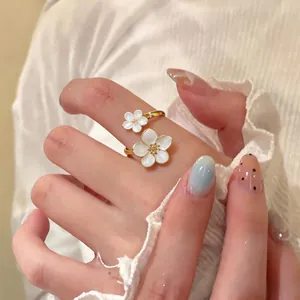 Vista dettagliata di un anello aperto in oro con eleganti fiori in smalto bianco su mano
