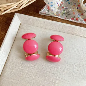 Gros plan de boucles d'oreilles en résine rose en forme de C avec un bord doré.