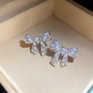 Close-up of elegant silver bow earrings with pearls and zircons in a beige jewelry box.