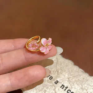Vista dettagliata di un elegante anello dorato con due fiori di ciliegio in smalto rosa al dito.