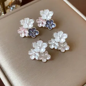 Elegant enamel flower stud earrings with white and pink petals displayed on jewelry cushion