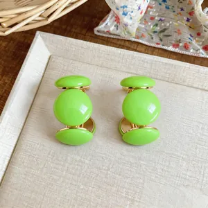 Détail des boucles d'oreilles clous en résine vert citron en forme de C doré.
