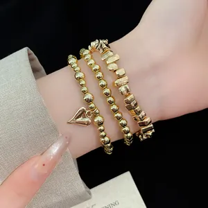 Primo piano di un set di tre braccialetti dorati con ciondolo a cuore sul polso.
