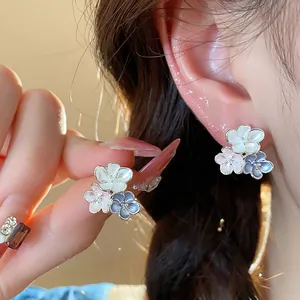 Close-up of elegant enamel flower stud earrings being worn on an ear and held by hand