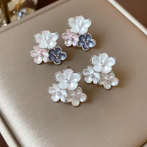 Detail view of dainty enamel flower stud earrings in white, pink, and blue finishes.