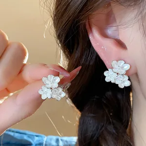 Detail of white enamel flower stud earrings with elegant silver needle design on ear