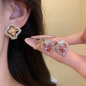 Close-up detail of sparkly pink strawberry earrings and luxury geometric stud earrings