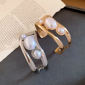 Detailed shot of elegant gold and silver hollow cuff bracelets featuring oval pearl inlays