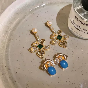 Elegant vintage gold-plated flower earrings with green and blue stones on a ceramic tray