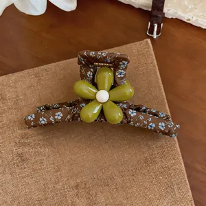 Detail view of a brown floral fabric hair claw clip with a green resin flower center.