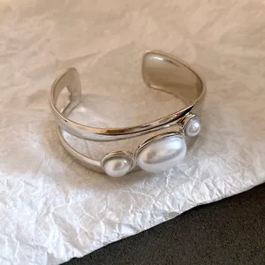 Detail of silver open cuff bracelet with oval and round pearls on textured paper