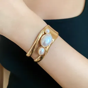 Detail view of a vintage hollow gold cuff bracelet featuring three elegant pearls on a wrist