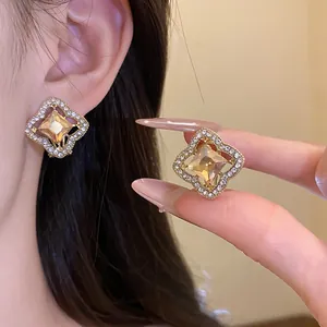 Close-up of elegant gold-toned flower earrings with central amber crystal and rhinestones.