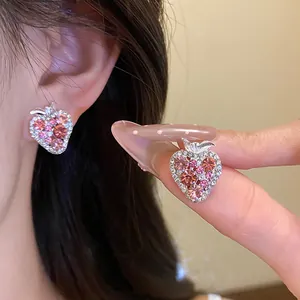 Detailed macro shot of sparkling pink rhinestone strawberry stud earrings on fingertips