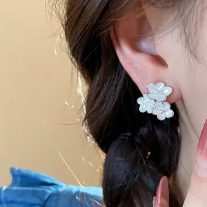Detail shot of white enamel flower stud earrings on model's ear for elegant look