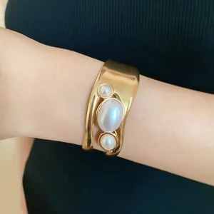 Detailed view of a gold-toned hollow cuff bracelet featuring three elegant oval pearls