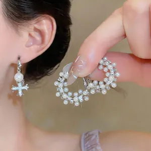Primo piano di eleganti orecchini a cerchio con perle, zirconi e ciondolo a croce.