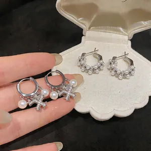 Primo piano di orecchini in argento con zirconi, perle e ciondoli a croce eleganti