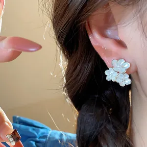 Detail of white enamel flower stud earrings shown on the ear for a delicate look