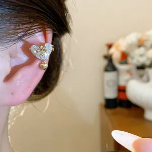 Detail view of an 18k gold plated heart zircon ear cuff with cross on a model's ear