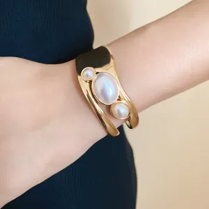 Close-up of a vintage gold-tone open cuff bracelet featuring three elegant oval pearls