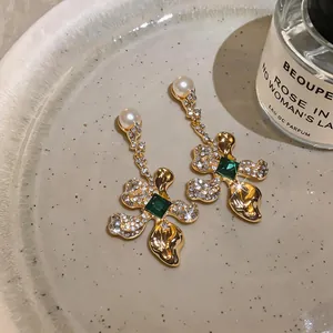 Close-up of vintage flower earrings with green stones and pearls on a ceramic plate