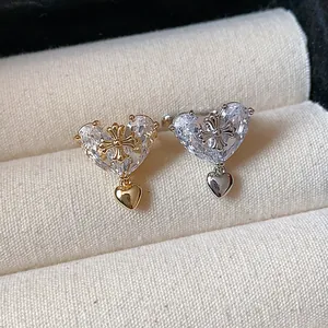 Close-up of heart-shaped zircon ear clips with cross detail in gold and silver finish