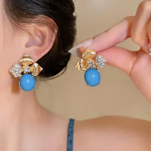 Close-up of floral stud earrings with blue stones and rhinestones worn by a model
