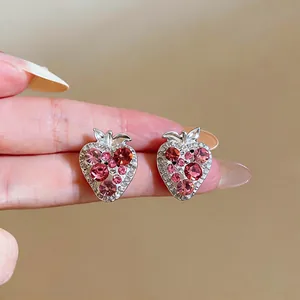 Detailed close-up of pink rhinestone-encrusted strawberry stud earrings with silver needles