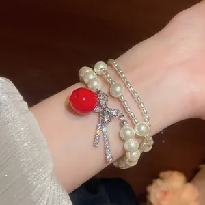 Close-up of multi-layer pearl bracelet with red apple and sparkling zircon bow.