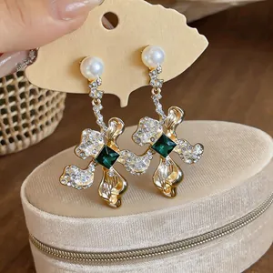 Close-up of elegant gold flower earrings with pearls and green emerald-style stones.