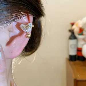 Close-up of 18k gold plated heart zircon ear cuff with cross detail and dangling heart
