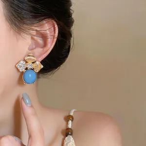 Detail of vintage flower stud earrings with blue stone and rhinestones on model's ear