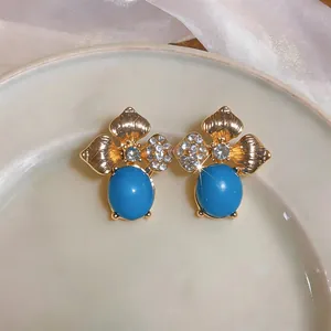 Macro view of elegant floral gold-tone stud earrings with oval blue stones and crystals.