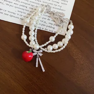 Detail of a multi-layer pearl bracelet with a red apple charm and a sparkling zircon bow