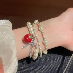 Close-up of multi-layer pearl bracelet with red apple and sparkling bow charm on wrist