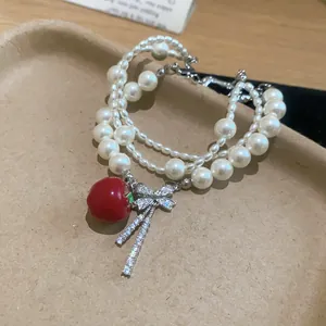 Detail view of a multi-layer pearl bracelet with a red apple and zircon bow charm.