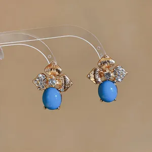 Close-up of gold-tone floral stud earrings with blue oval stones and rhinestones.