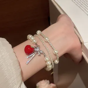 Elegant detail of a multi-layer pearl bracelet featuring a zircon bow and red apple charm.