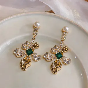 Elegant floral earrings featuring emerald green stones, rhinestones, and pearls. Macro detail.