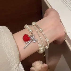Close-up of elegant multi-layer pearl bracelet with red apple charm and zircon bow