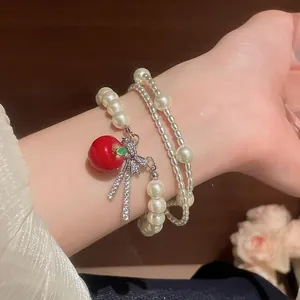 Detailed view of multilayer pearl bracelet with zircon bow and red apple charm