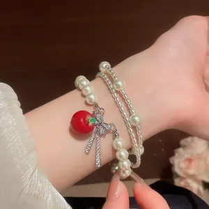 Close-up of a multi-layer pearl bracelet with a red apple charm and rhinestone bow