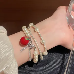 Close-up of a multi-layer pearl bracelet with a red apple and zircon bow charm.