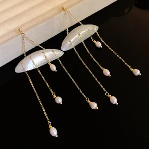 Detailed close-up of shell and freshwater pearl tassel earrings on black surface