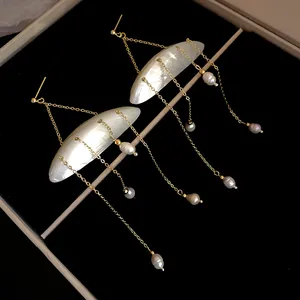 Close-up of shell and freshwater pearl tassel earrings with delicate gold-plated chains.